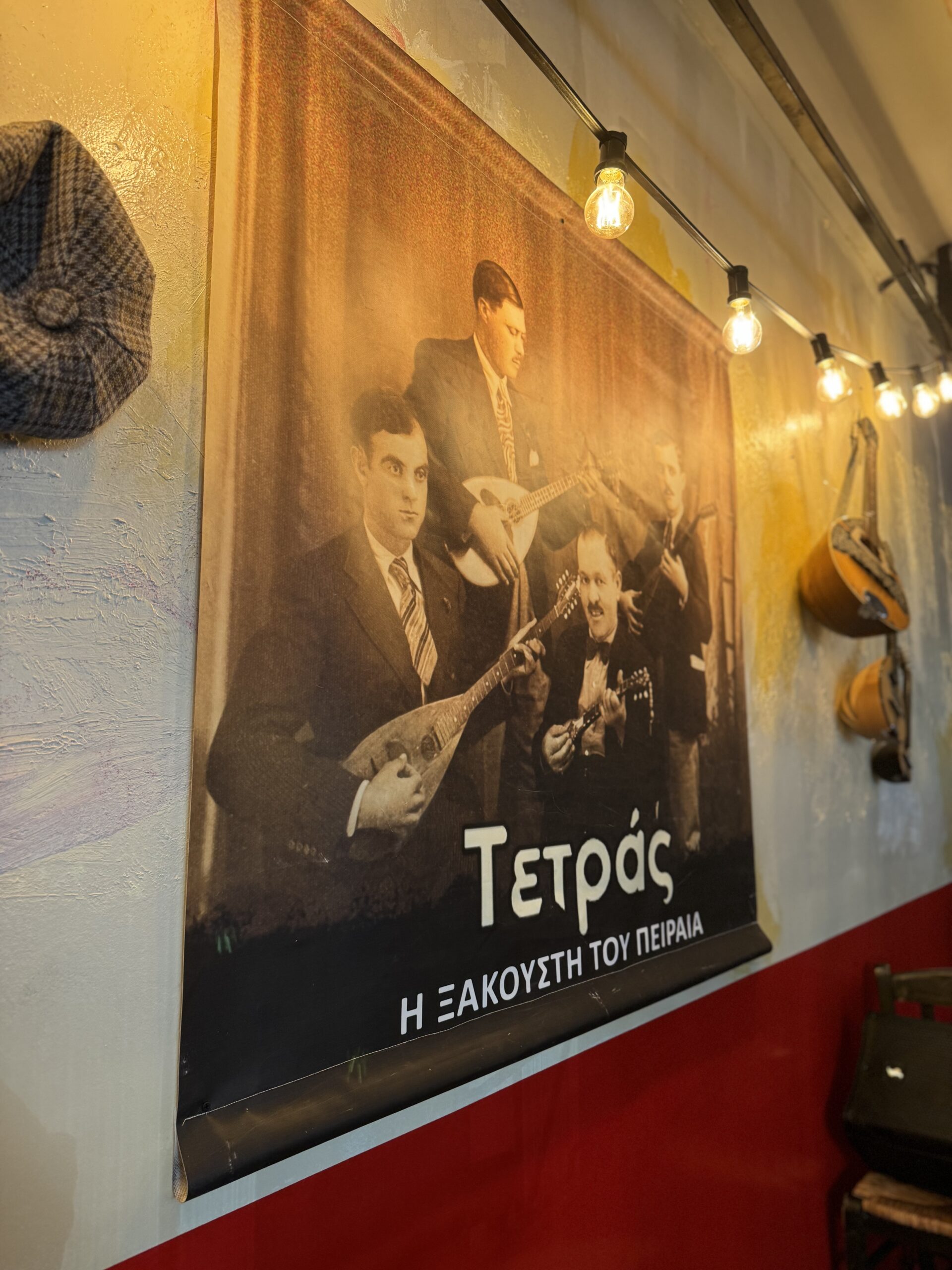 Η αφίσα της Τετράδας του Πειραιά, με καπέλα και μπαγλαμάδες κρεμασμένα στον τοίχο